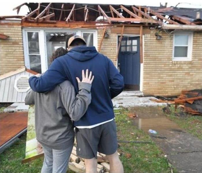 Storm damage to home and woman and man hugging